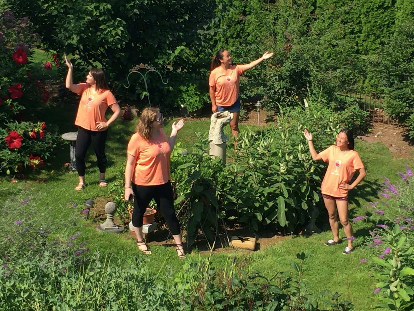 Group of four young ladies in statue garden enjoying friends' retreat. Wearing matching orange tee shirts.
