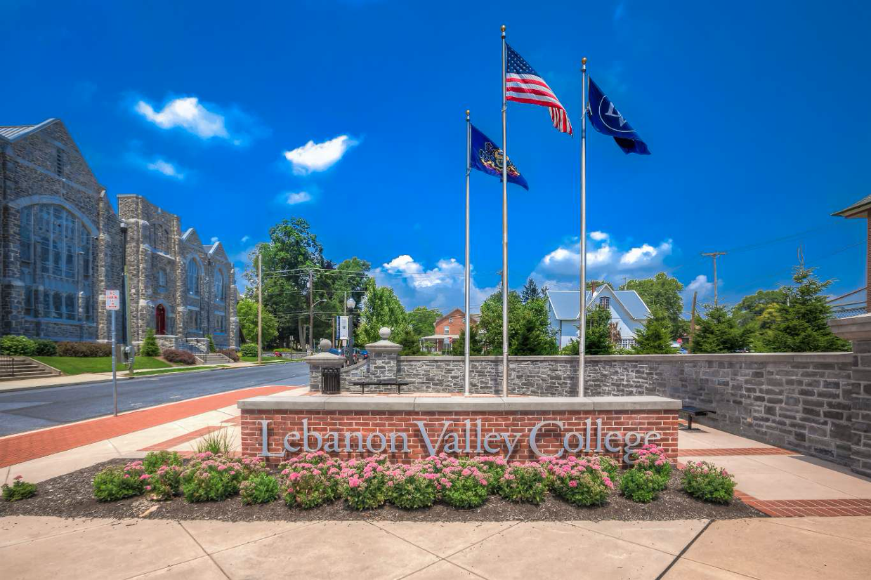 Entrance to Lebanon Valley College. Sign with flags, blue sky in background.