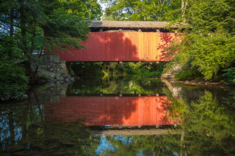 red covered bridge spanning a creek with bridge reflected in water