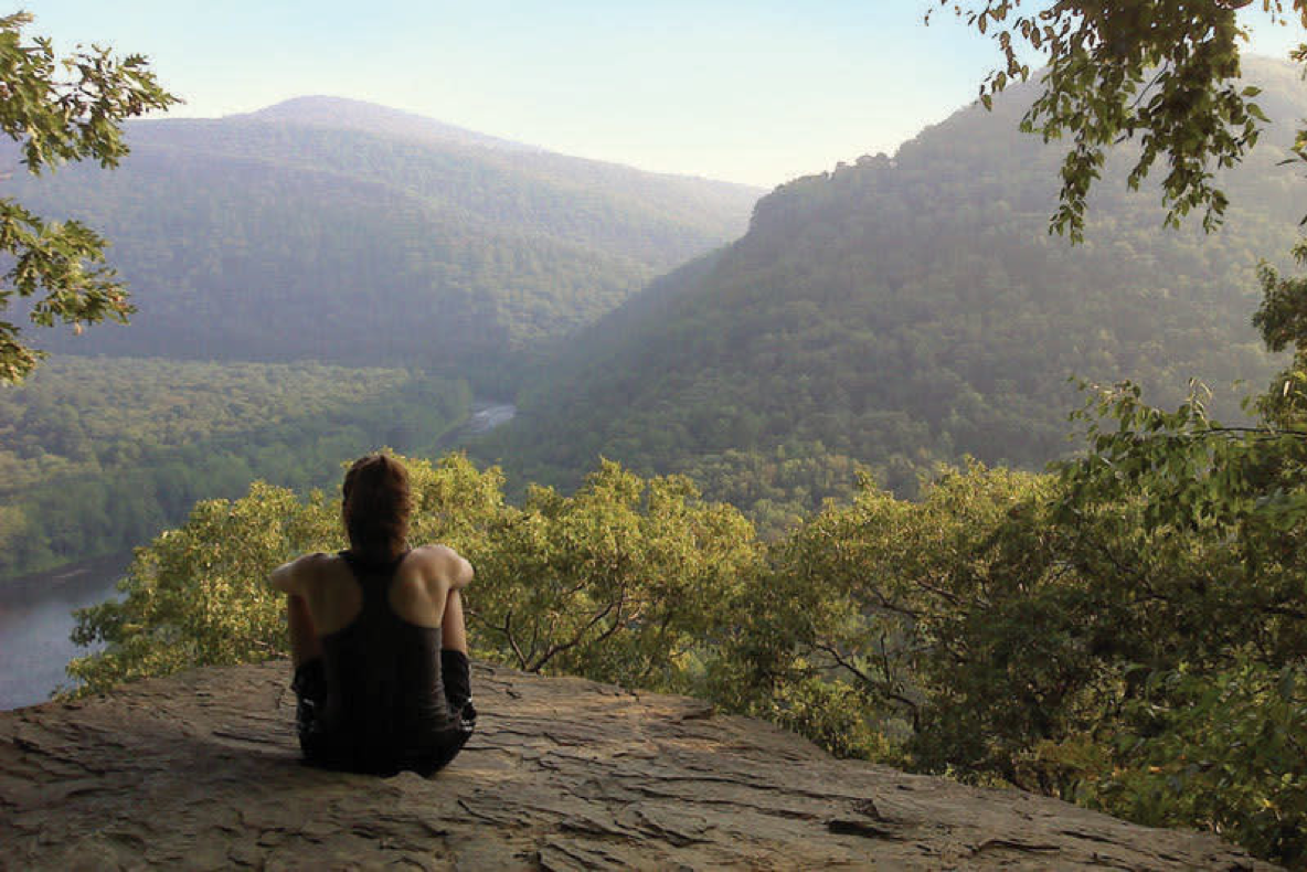 person sitting on a ledge overlooking mountains and river
