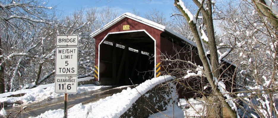 Covered bridge in forest scene shrouded in freshly fallen snow with bright blue sky