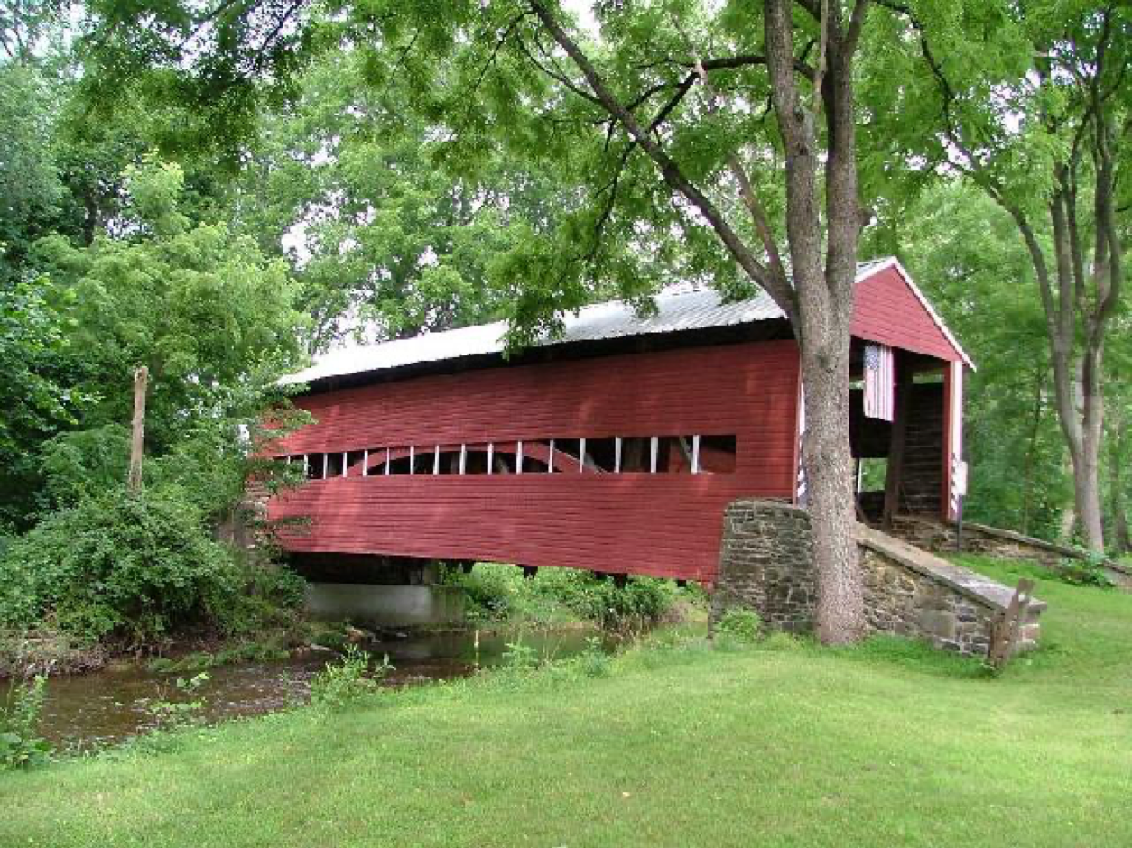 Long, red covered bridge with flag hanging from front. This bridge has a long line of windows along its sides.