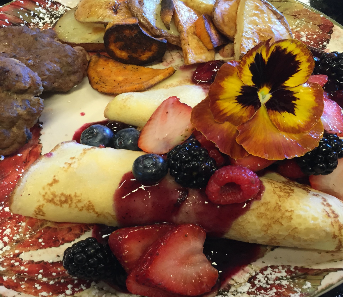 Breakfast at Annville Inn. Crepes with a warm berry sauce, home made sausage, oven roasted potato medly. Garnished by a unique colorful pansy.
