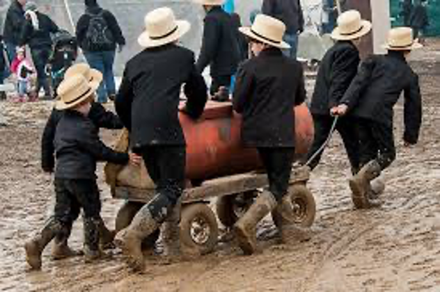 Six Amish boys move a tank on wheels through the mud