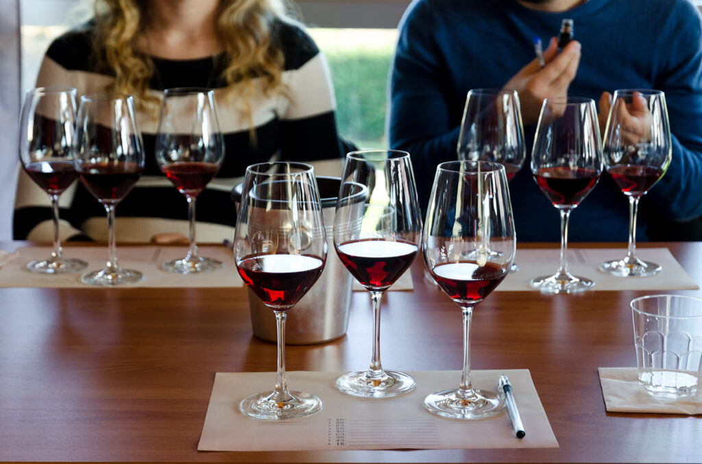 Photo of nine glasses of wine being tasted by a couple in a wine class. There is also note paper on the table the glasses are sitting on...for taking notes.