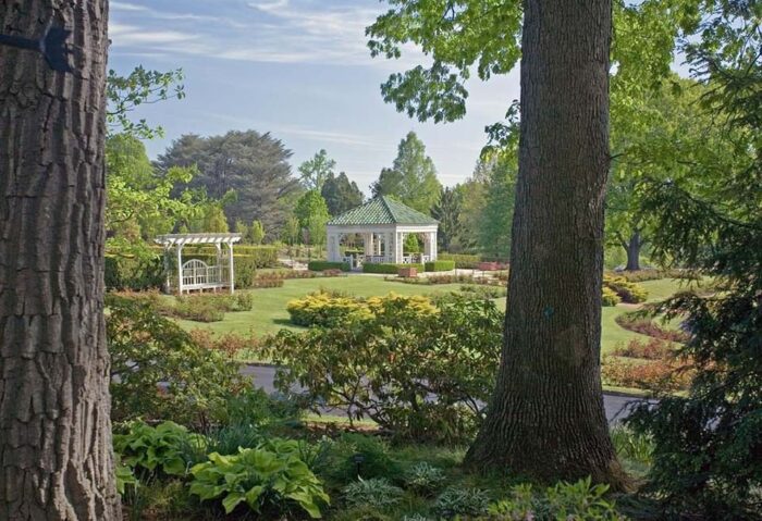 Beautiful image of a garden gazebo and bench with a walking path and two trees in foreground.