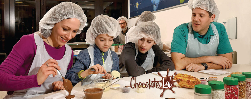 Mom and Dad and two kids at the Chocolate Lab within the Hershey Story Museum. They are creating their own candy bars. They are wearing hair restraints, just like in the real chocolate factory!
