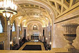 POhoto shows the massive 3-storey lobby with arched ceiling and gold leaf.  In the foreground is a tall urn.