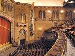 Sweeping view along the balcony and lower  front tier of seating as well as image shows part of the stage (on left side).