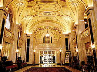Grand lobby is shown in this photo showing massive arched ceilings and engpaged wall columns.  Colors are chiefly gold leaf and white.