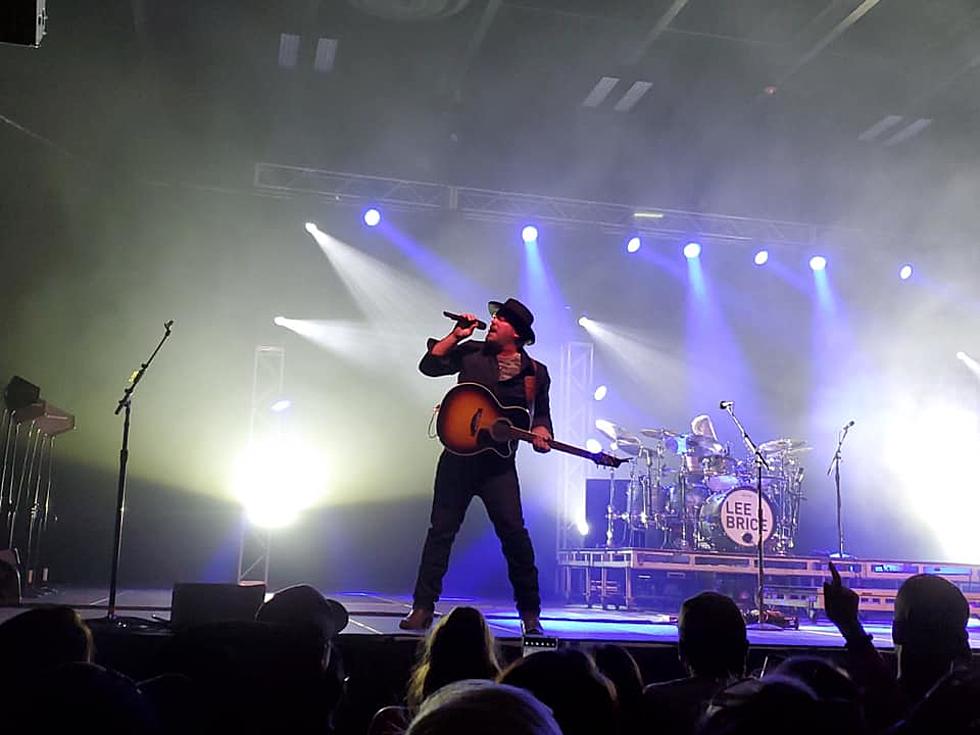 Lee Brice in concert on stage. Behind him is the drummer with a full drum set, and bright white lights, while the rest of the stage is in purple/blue. In foreground is a large crowd. He will be at Holly Casino Near Hershey this summer.