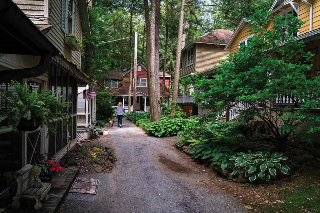 Image shows a "street" in Mt. Gretna near Hershey, Pa.  A lady is walking a dog down the very narrow street, lined on both sides with large cottages with huge porches!