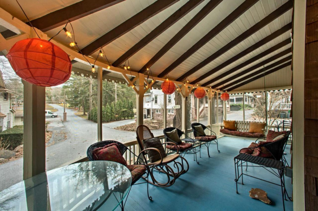 Image shows one of the cottages in Mt. Gretna, near Hershey, Pa.  It is a view from inside the porch, showing a very large beamed porch, screened in, with a bentwood rocker, a porch swing and several other chairs.