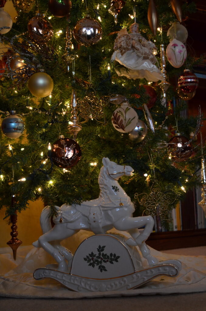 Porcelain rocking horse sitting under a decorated Christmas Tree. 