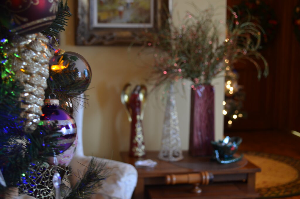 Christmas Tree with ornaments and lights, with a table in the background with an angel figuring.