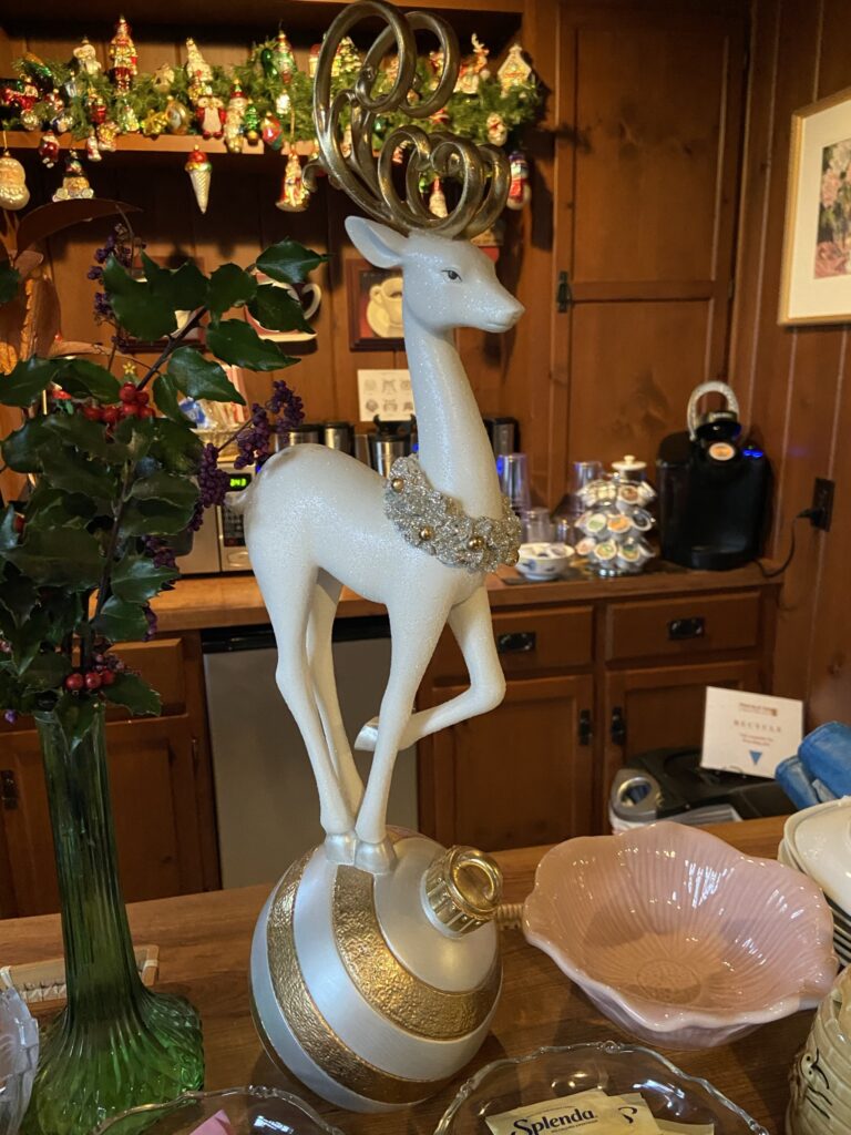 Cozy coffee bar with a White Reindeer Figuring and Christmas decorations. Christmas Garland with Christmas Ornaments in background.