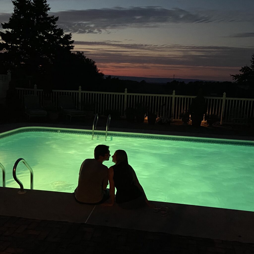 Silhouette photo of a couple sitting next to a pool while the sun sets.