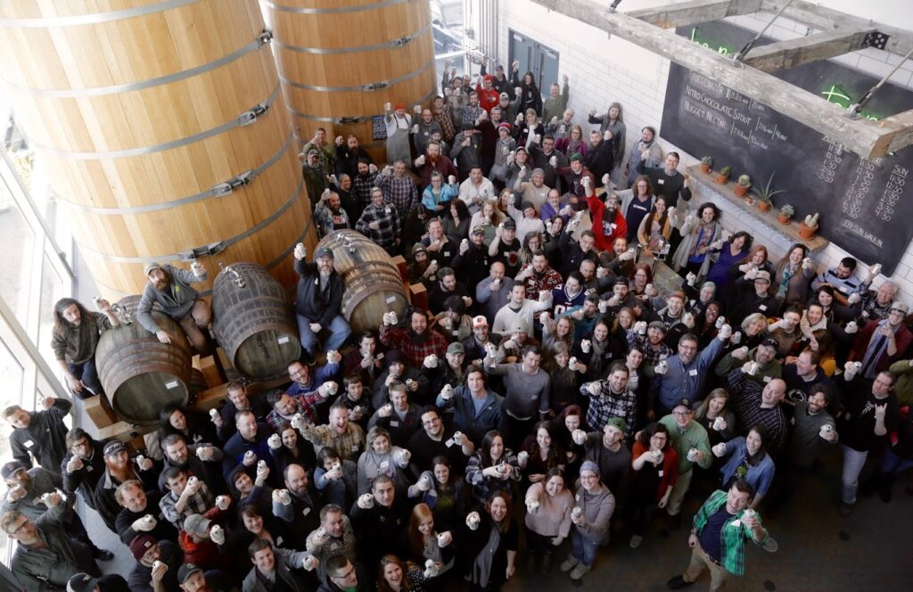 Image taken from several stories up above the  Tröegs brewery floor. Shows 170 employees grouped around giant tanks of the brewery.